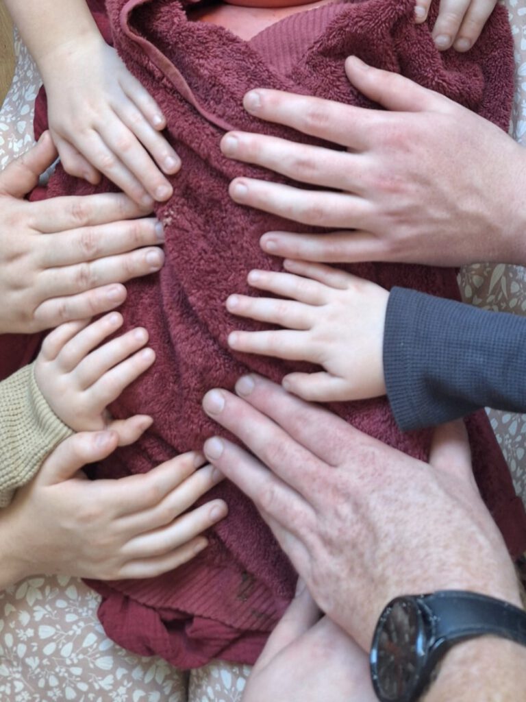 Die Hände einer Familie liegen auf dem Babykörper, welcher bei einer stillen Geburt zur Welt kam.