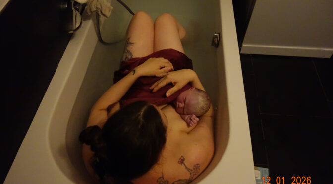 Eine Mutter sitzt mit ihrem Neugeborenen in der Badewanne nach einer erfolgreichen Alleingeburt.